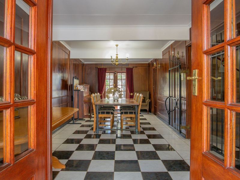 Spacious dining room featuring classic wooden wall paneling, distinctive checkered floor tiles, and elegant double door access.