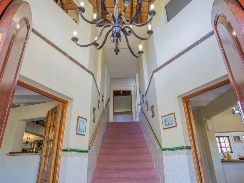 Spacious double-volume entrance hall featuring a grand staircase, exposed thatch ceiling, and a decorative wrought iron chandelier, providing a welcoming and character-filled arrival area.