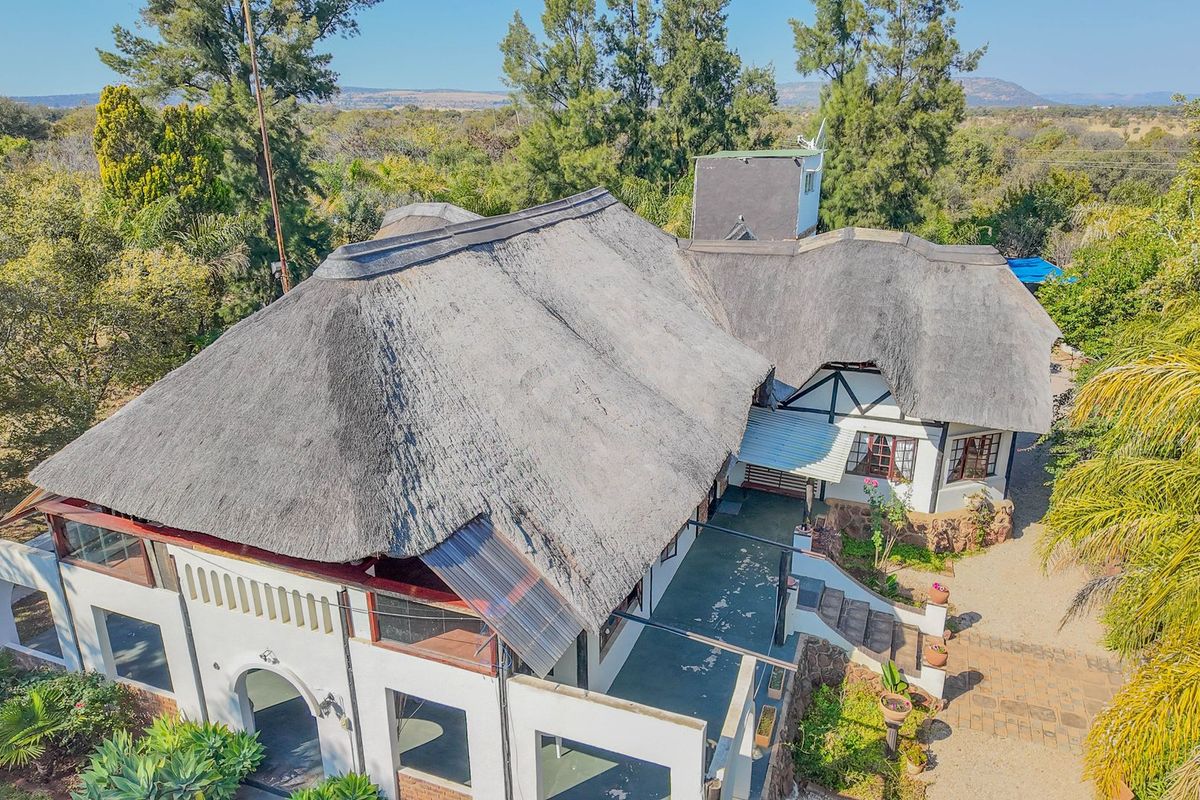 Aerial view of a large small holding property featuring a traditional thatch roof, stone accents, and an expansive surrounding garden landscape.