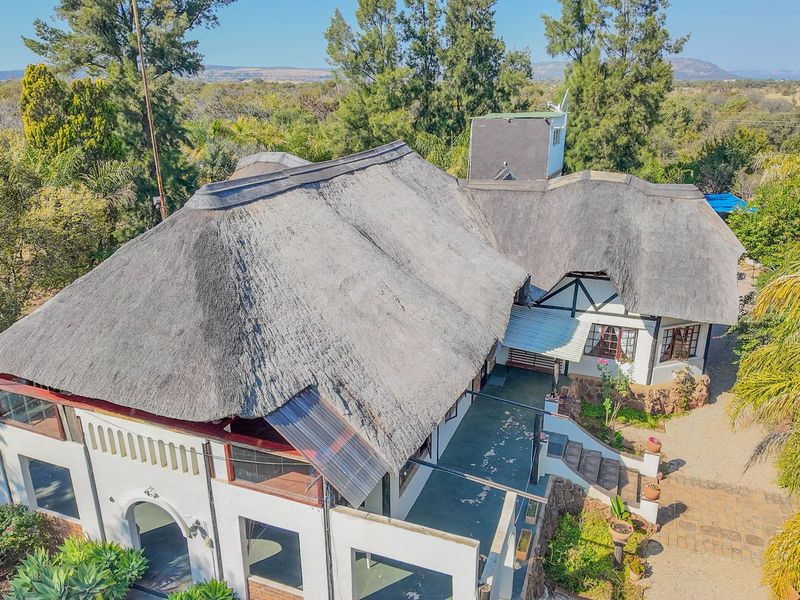 Aerial view of a large small holding property featuring a traditional thatch roof, stone accents, and an expansive surrounding garden landscape.