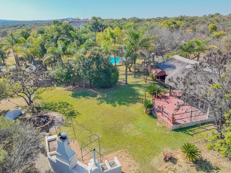 Aerial view of a small holding property featuring a thatched roof dwelling, a raised wooden deck, an outdoor fireplace, and a swimming pool.