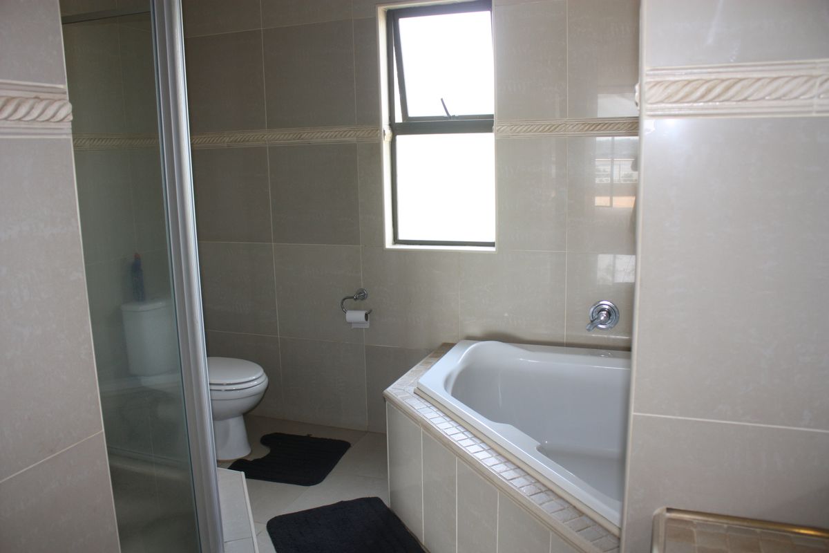A functional bathroom featuring a built-in bathtub, a separate shower enclosure, and a toilet, finished with neutral wall and floor tiling.