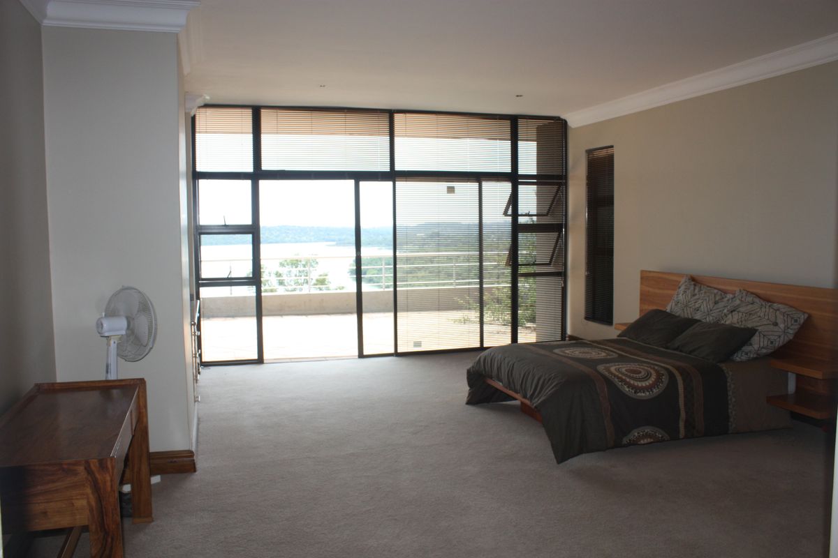 Spacious bedroom featuring large sliding glass doors that open onto a balcony with scenic views, complemented by neutral carpeting and built-in headboard.
