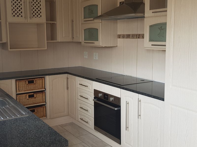 A functional kitchen featuring light wood-grain cabinetry, granite countertops, a double sink, and integrated appliances including an oven, hob, and extractor fan.