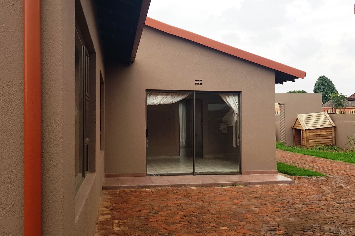 Rear view of the property featuring a paved courtyard, sliding glass door access, and a well-maintained exterior facade with tiled roofing.