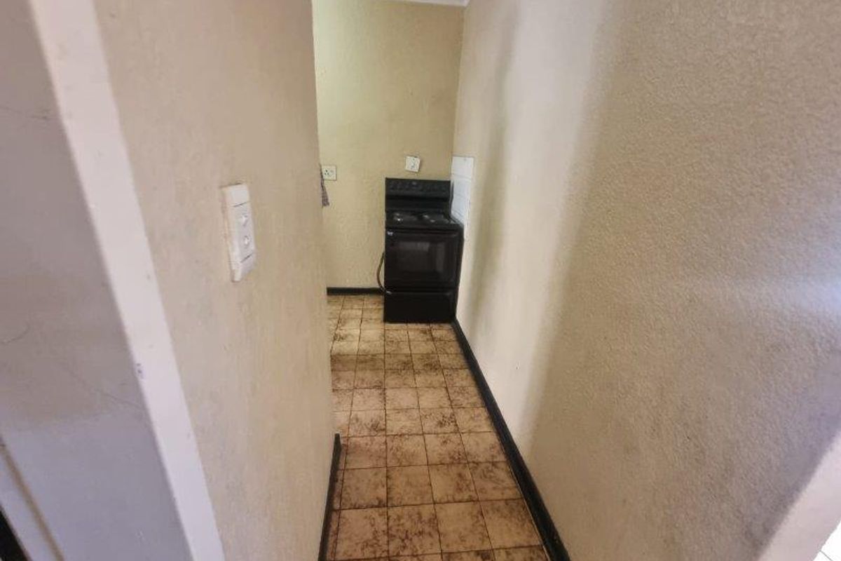 A narrow kitchen area featuring tiled flooring and a freestanding stove, requiring cosmetic updates and maintenance to improve the overall finish.