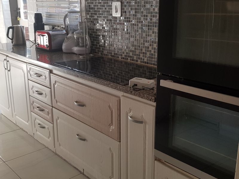 A functional kitchen featuring white cabinetry, granite countertops, a mosaic tile backsplash, and a built-in double oven with an integrated electric hob.