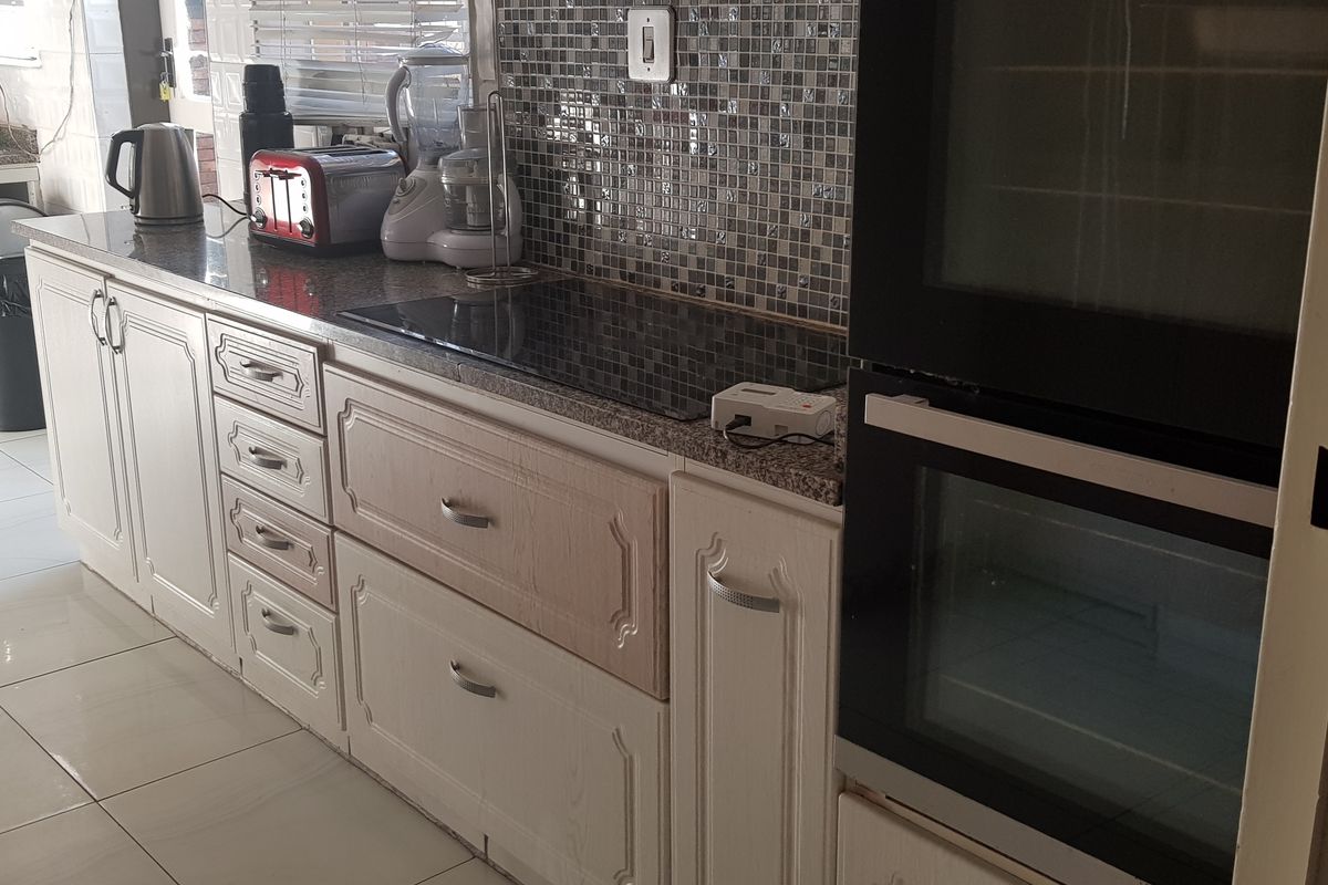 A functional kitchen featuring white cabinetry, granite countertops, a mosaic tile backsplash, and a built-in double oven with an integrated electric hob.