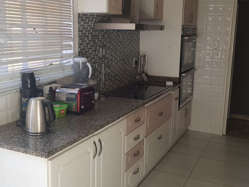 A functional kitchen featuring granite countertops, mosaic tile backsplash, built-in oven, electric cooktop, and tiled flooring with ample cabinetry.