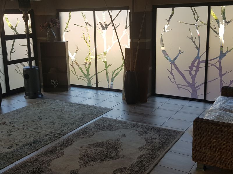 A living room featuring large sliding glass doors with decorative tree-patterned privacy film and neutral tiled flooring.