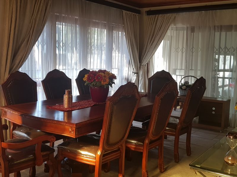 A formal dining room featuring large windows with security gates, neutral curtains, and tiled flooring, providing a bright and traditional space for family meals.