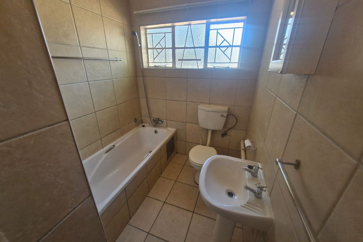 A functional bathroom featuring a bathtub, pedestal basin, and toilet with neutral wall and floor tiling.
