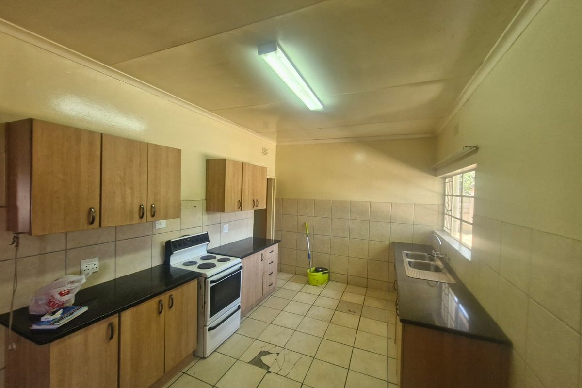 A functional kitchen featuring laminate cabinetry, granite countertops, a double bowl sink, and a freestanding stove, with tiled flooring and splashbacks throughout.