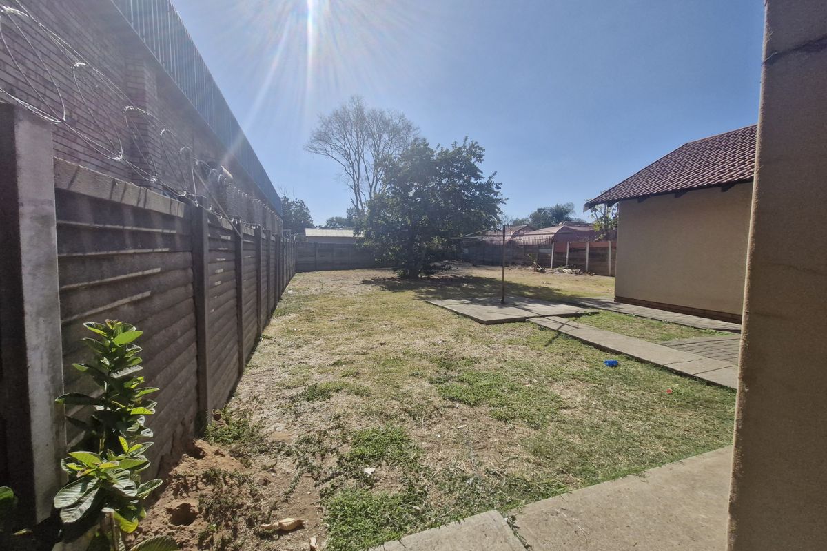 A spacious rear garden area featuring a precast concrete boundary wall with security razor wire and a paved walkway leading to the main structure.