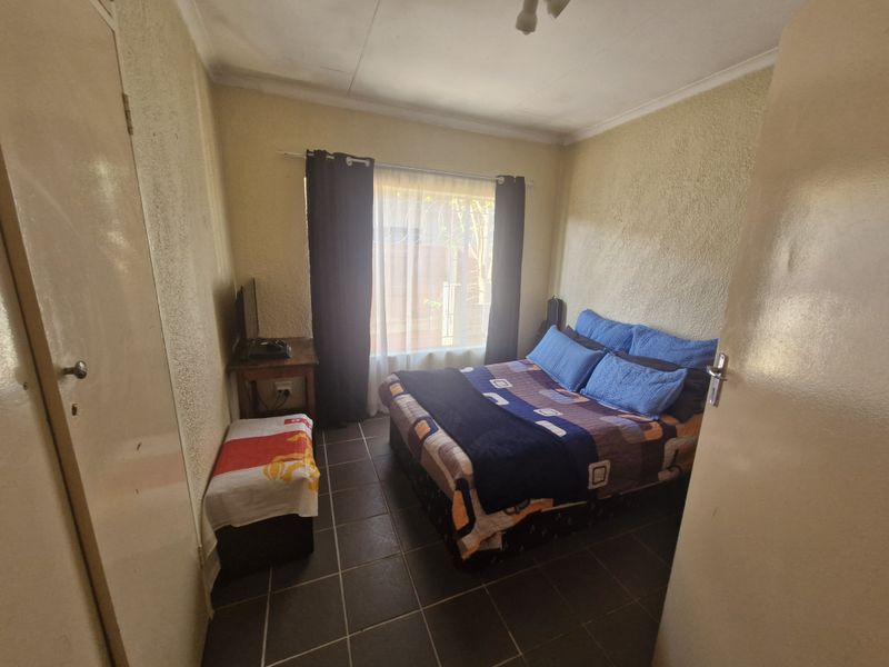 A compact bedroom featuring tiled flooring and a built-in cupboard, requiring cosmetic updates to the wall finishes and ceiling.