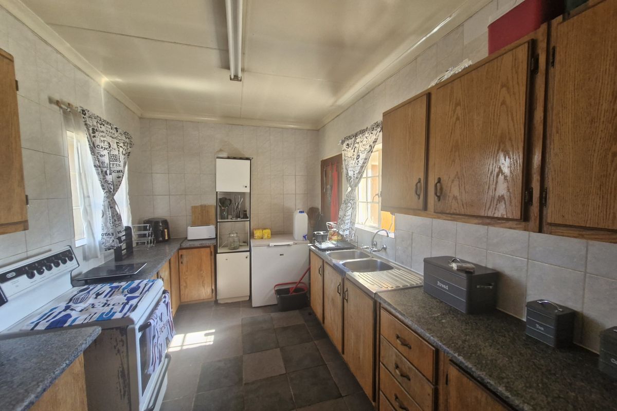 A functional kitchen featuring wooden cabinetry, tiled splashbacks, and a double bowl stainless steel sink, offering potential for a modern renovation.