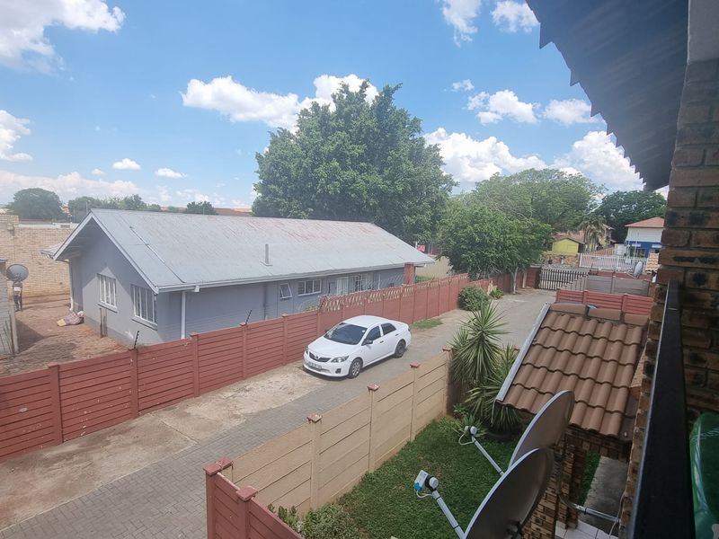 Elevated view overlooking a residential complex courtyard featuring paved driveways, precast boundary walls, and surrounding properties.