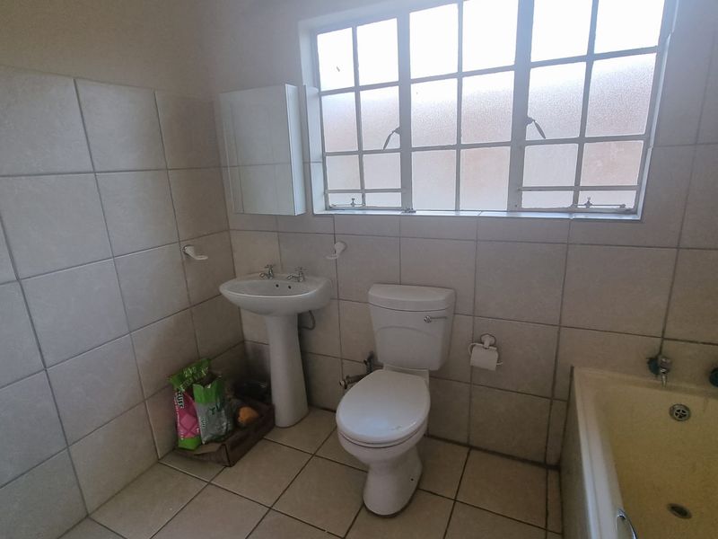 A functional bathroom featuring a pedestal basin, toilet, and bathtub with tiled finishes throughout, requiring cosmetic updates to modernize the space.