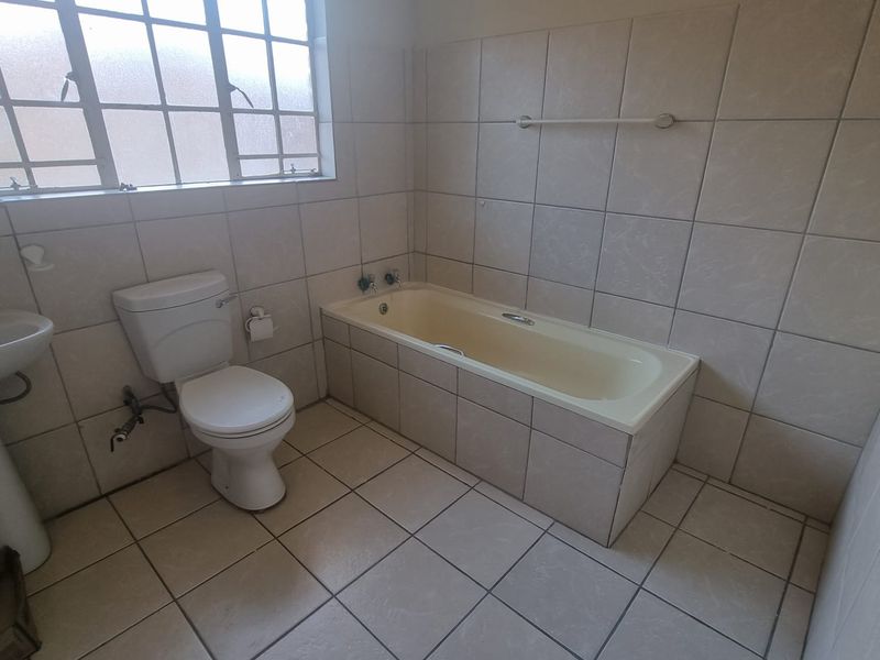 A functional bathroom featuring a tiled floor and walls, a pedestal basin, a toilet, and a built-in bathtub.