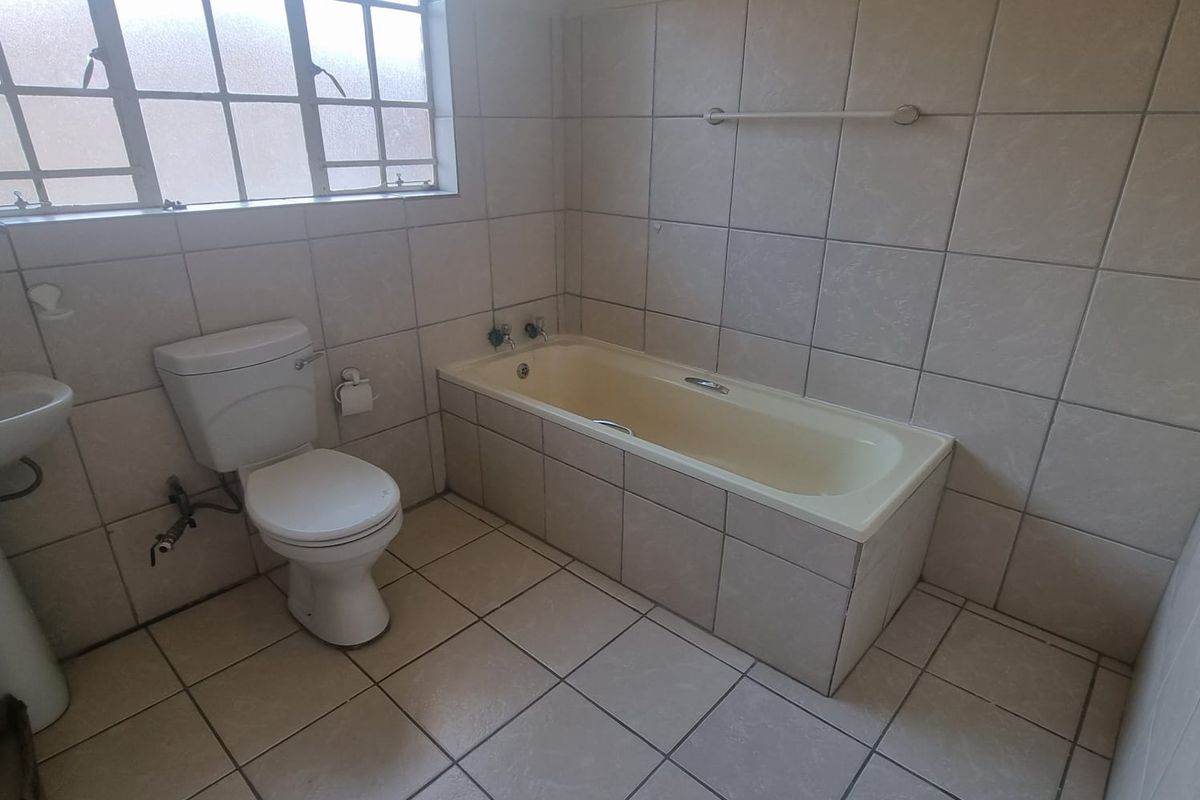 A functional bathroom featuring a tiled floor and walls, a pedestal basin, a toilet, and a built-in bathtub.