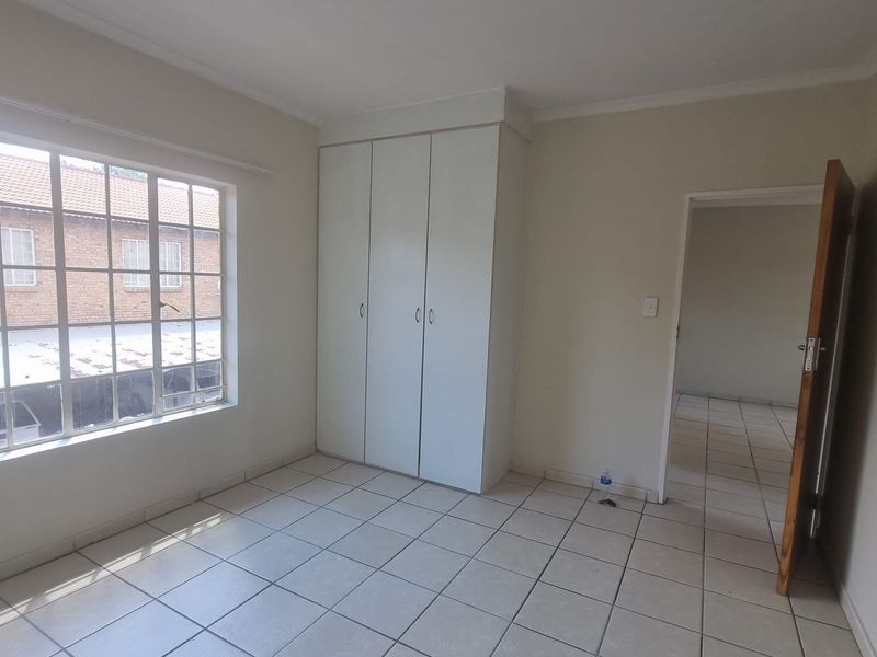 An empty bedroom featuring neutral tiled flooring, built-in cupboards, and a window with security bars, offering a clean and functional space.