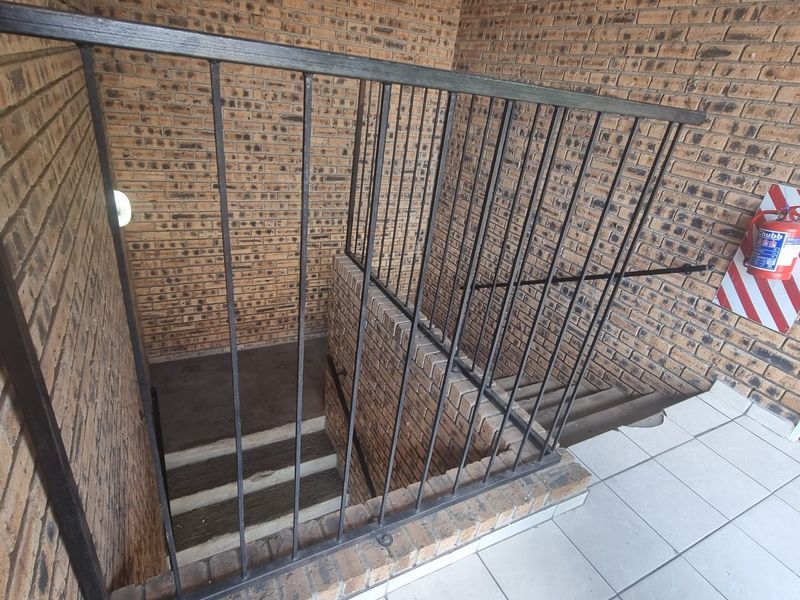 A functional apartment building stairwell featuring exposed brick walls, a metal safety balustrade, and tiled flooring with a wall-mounted fire extinguisher.