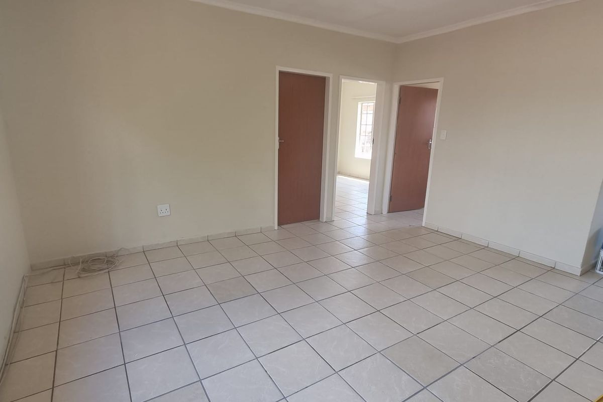 A bright, empty living area featuring neutral tiled flooring, clean walls, and access to adjacent rooms through internal doors.
