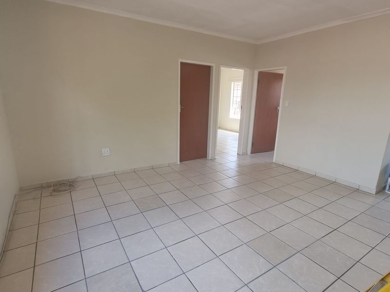 A bright, empty living area featuring neutral tiled flooring, clean walls, and access to adjacent rooms through internal doors.