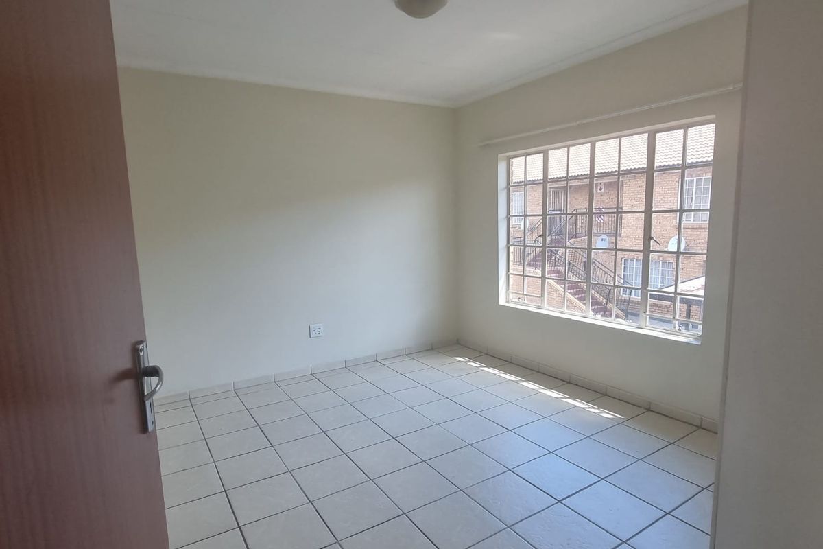 A bright, empty bedroom featuring neutral tiled flooring, a large multi-pane window, and a simple ceiling light fixture, ready for personalization.