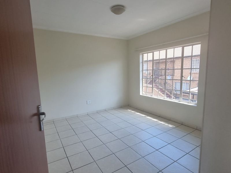 A bright, empty bedroom featuring neutral tiled flooring, a large multi-pane window, and a simple ceiling light fixture, ready for personalization.