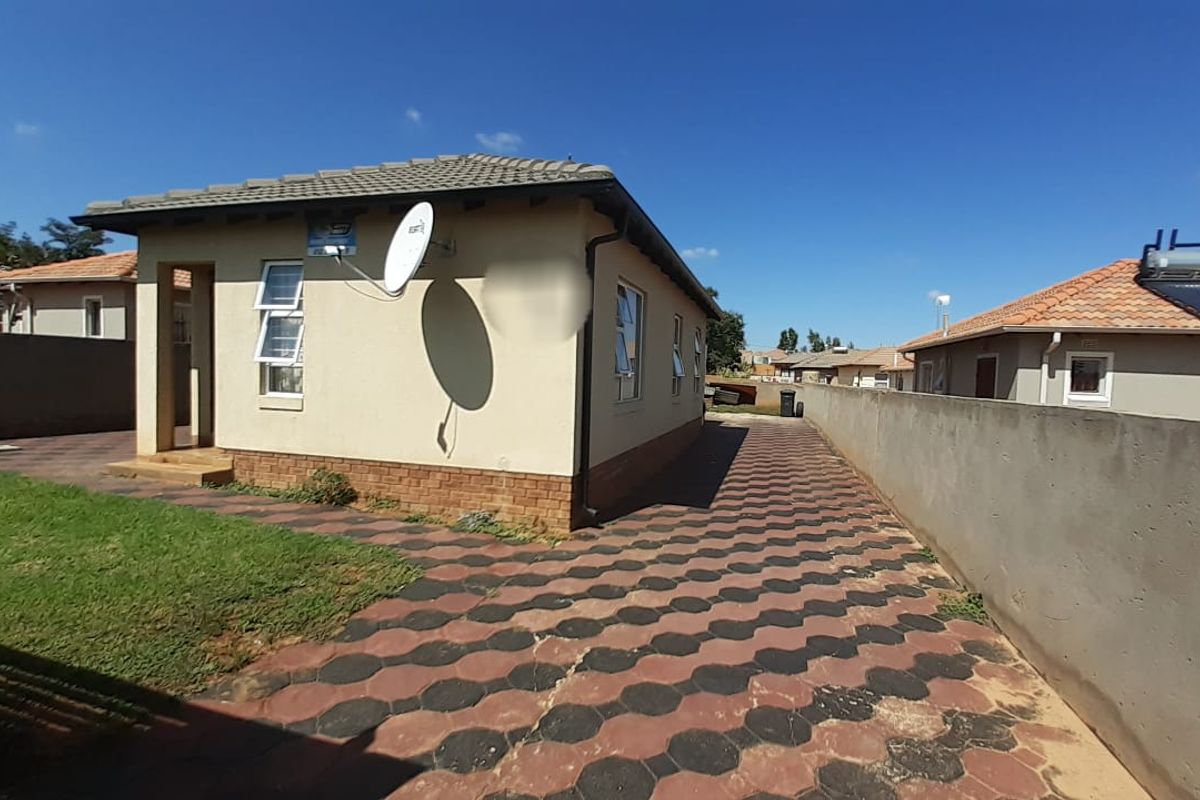Rear view of a residential house featuring a tiled roof, paved exterior area, and boundary walling.