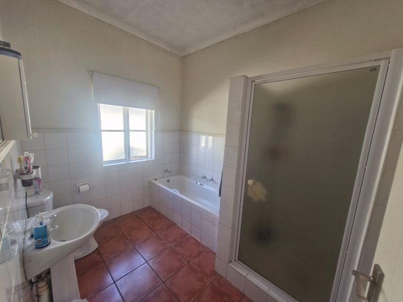 A functional bathroom featuring a pedestal basin, built-in bathtub, and a separate shower enclosure with tiled finishes.