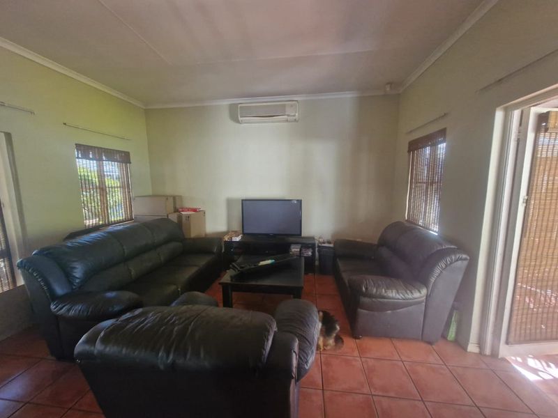 A living room featuring terracotta floor tiles, a wall-mounted split-system air conditioner, and natural light through timber-blinded windows.