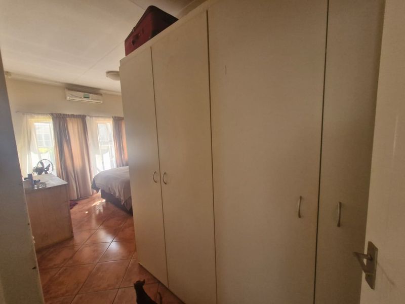 A bedroom featuring built-in cupboards, tiled flooring, and a wall-mounted air conditioning unit.