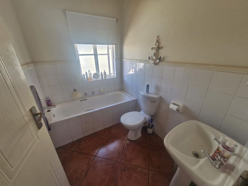 A functional bathroom featuring a built-in bathtub, pedestal basin, toilet, and tiled flooring with partial wall tiling.