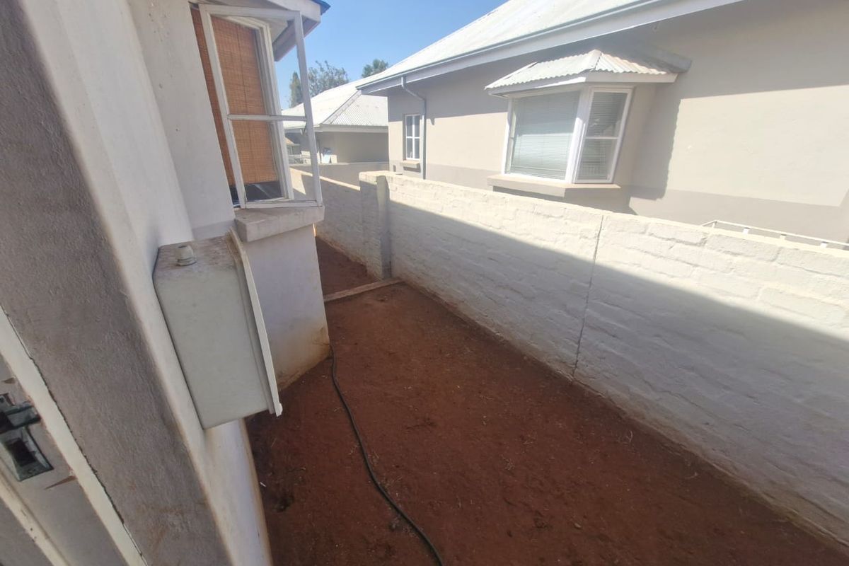 A side passage or rear exterior area featuring a boundary wall, exposed earth ground, and views of the adjacent townhouse structure.