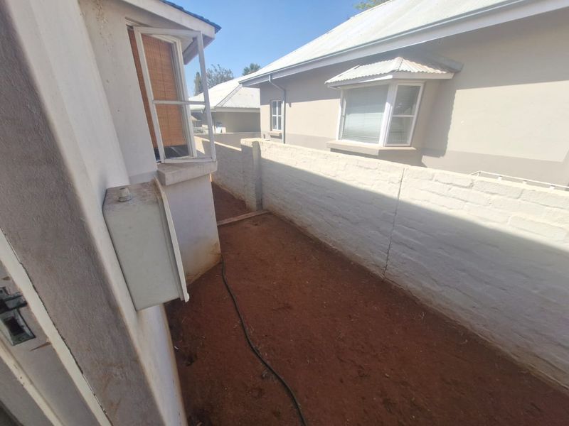A side passage or rear exterior area featuring a boundary wall, exposed earth ground, and views of the adjacent townhouse structure.
