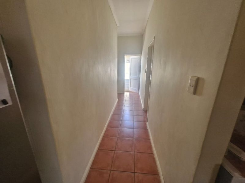 A simple, empty hallway featuring tiled flooring and neutral wall finishes, providing access to other areas of the townhouse.