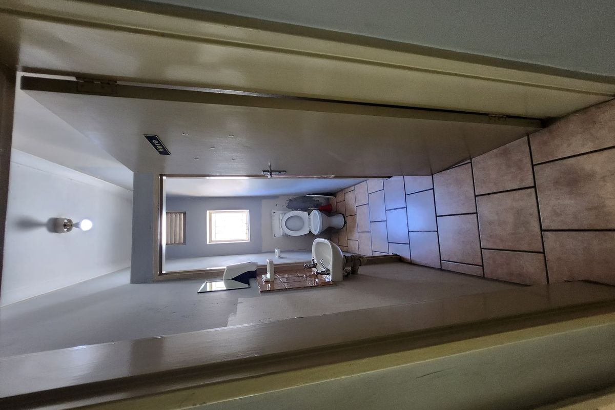 A functional industrial restroom featuring a wall-mounted basin, toilet, and tiled flooring, accessible via a standard door.