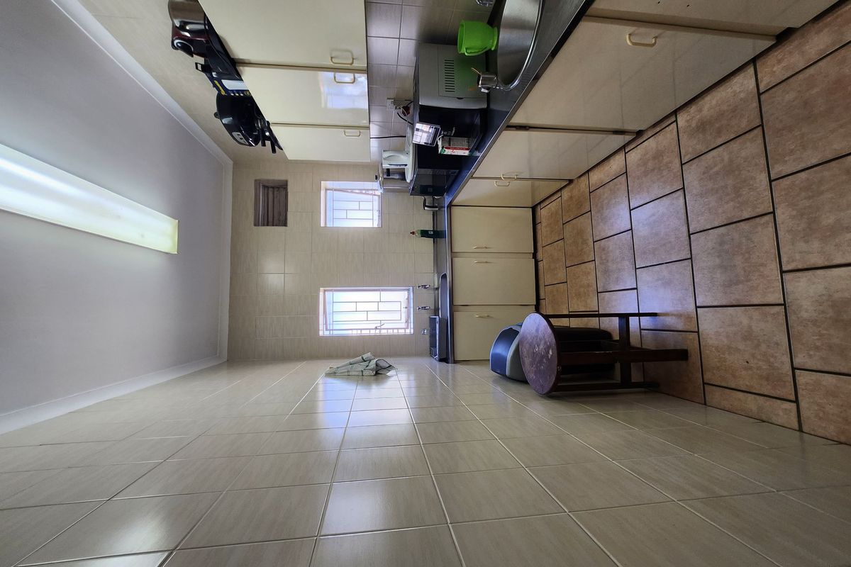 A functional galley-style kitchen featuring tiled walls, ample cabinetry, dual stainless steel sinks, and tiled flooring, providing a practical workspace.