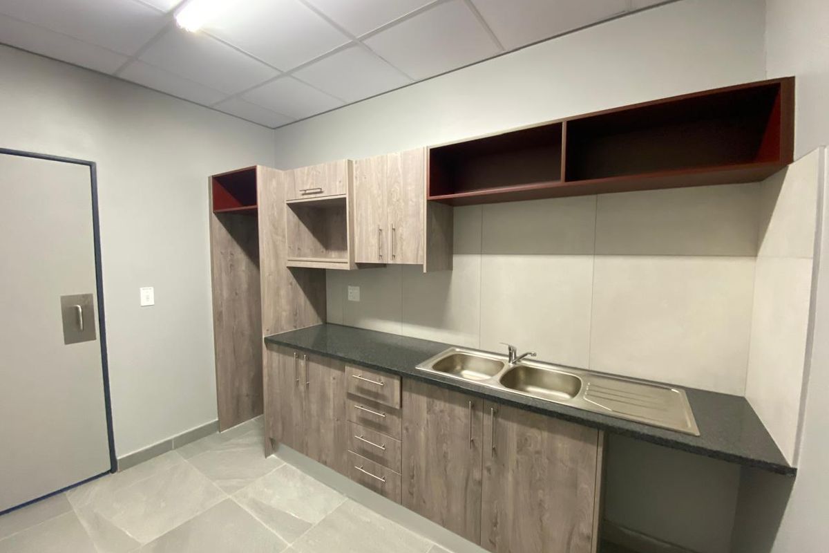 A functional kitchenette area featuring wood-look cabinetry, a double stainless steel sink, dark laminate countertops, and a suspended acoustic tile ceiling.