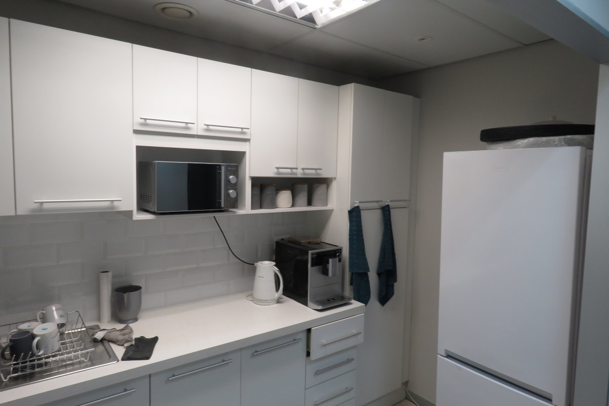 A compact office kitchenette featuring white cabinetry, subway tile backsplash, integrated microwave, and a freestanding refrigerator.