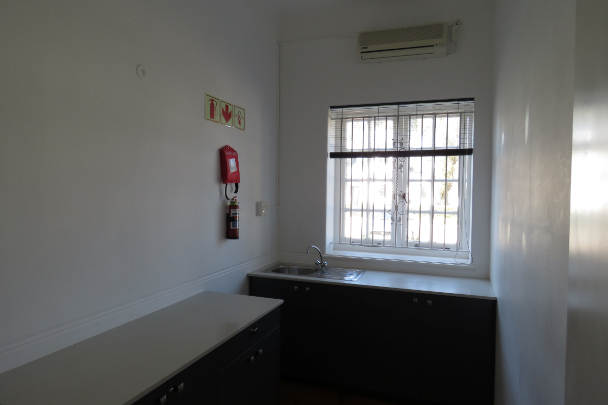 A functional office kitchenette featuring dark cabinetry, a stainless steel sink, and a wall-mounted fire extinguisher.