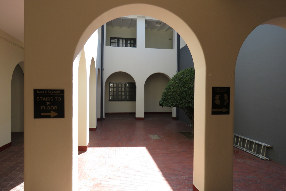 A covered outdoor courtyard area featuring arched walkways, brick paving, and directional signage within a commercial office complex.