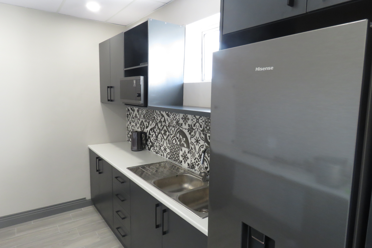 Modern office kitchenette featuring dark cabinetry, patterned tile backsplash, stainless steel double sink, and integrated microwave.