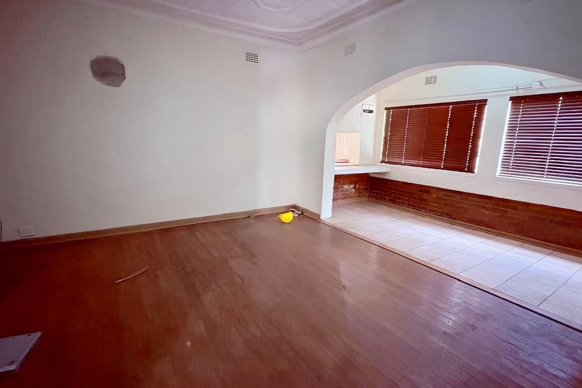An empty living area featuring an arched transition to an adjacent tiled space with brick accents and window blinds.