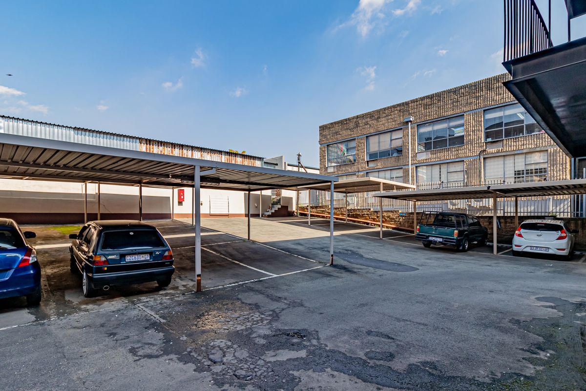 Exterior view of the office property featuring a paved parking area with covered carports and multi-story brick building facade.