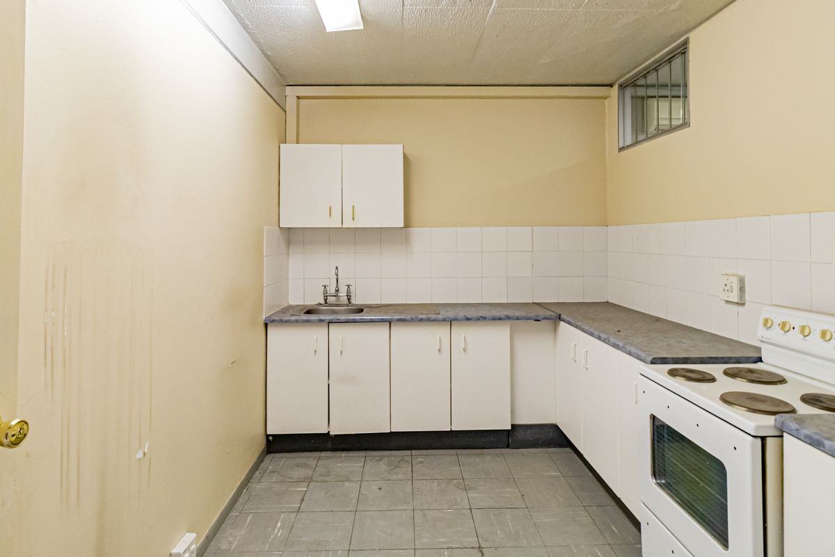 A functional kitchenette featuring white cabinetry, a stainless steel sink, tiled splashback, and a built-in electric stove.