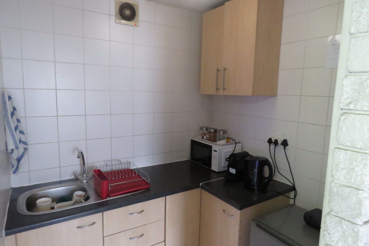 Compact kitchenette featuring light wood cabinetry, tiled splashbacks, a stainless steel sink, and an integrated extractor fan.