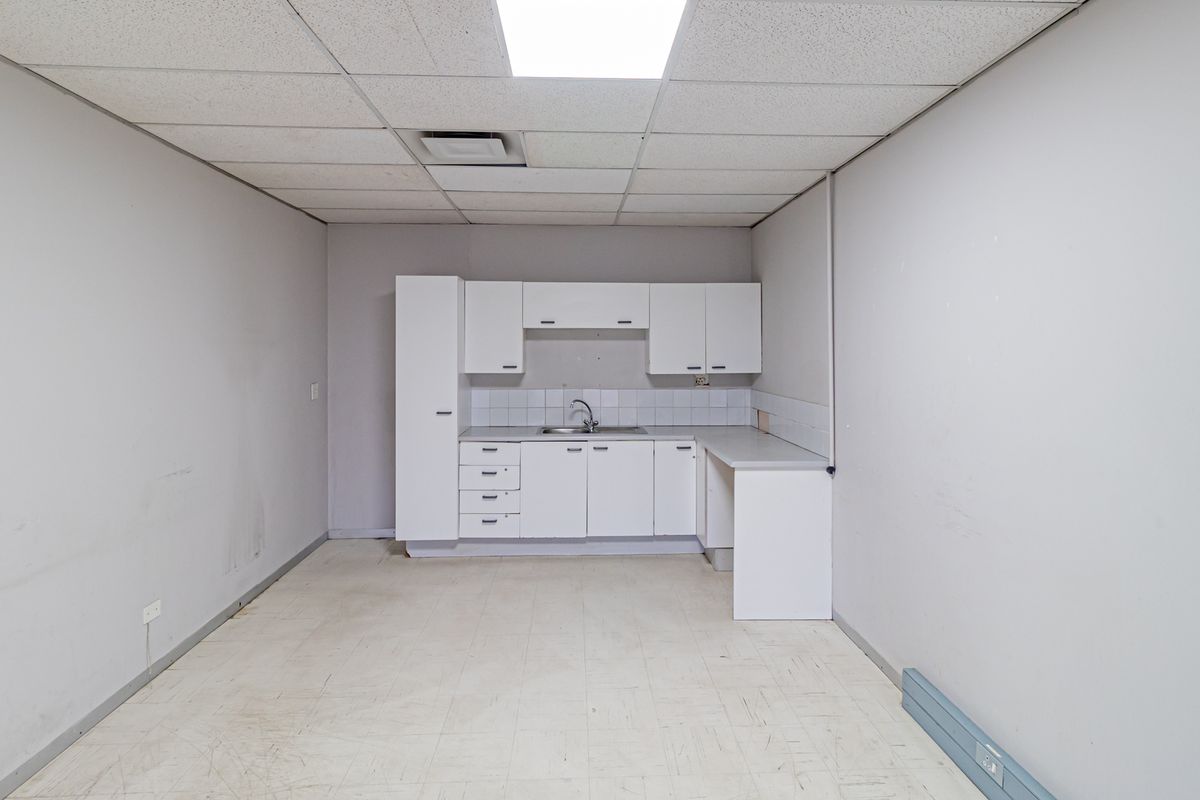 A functional office kitchenette featuring white cabinetry, a stainless steel sink, and a drop ceiling with integrated lighting.